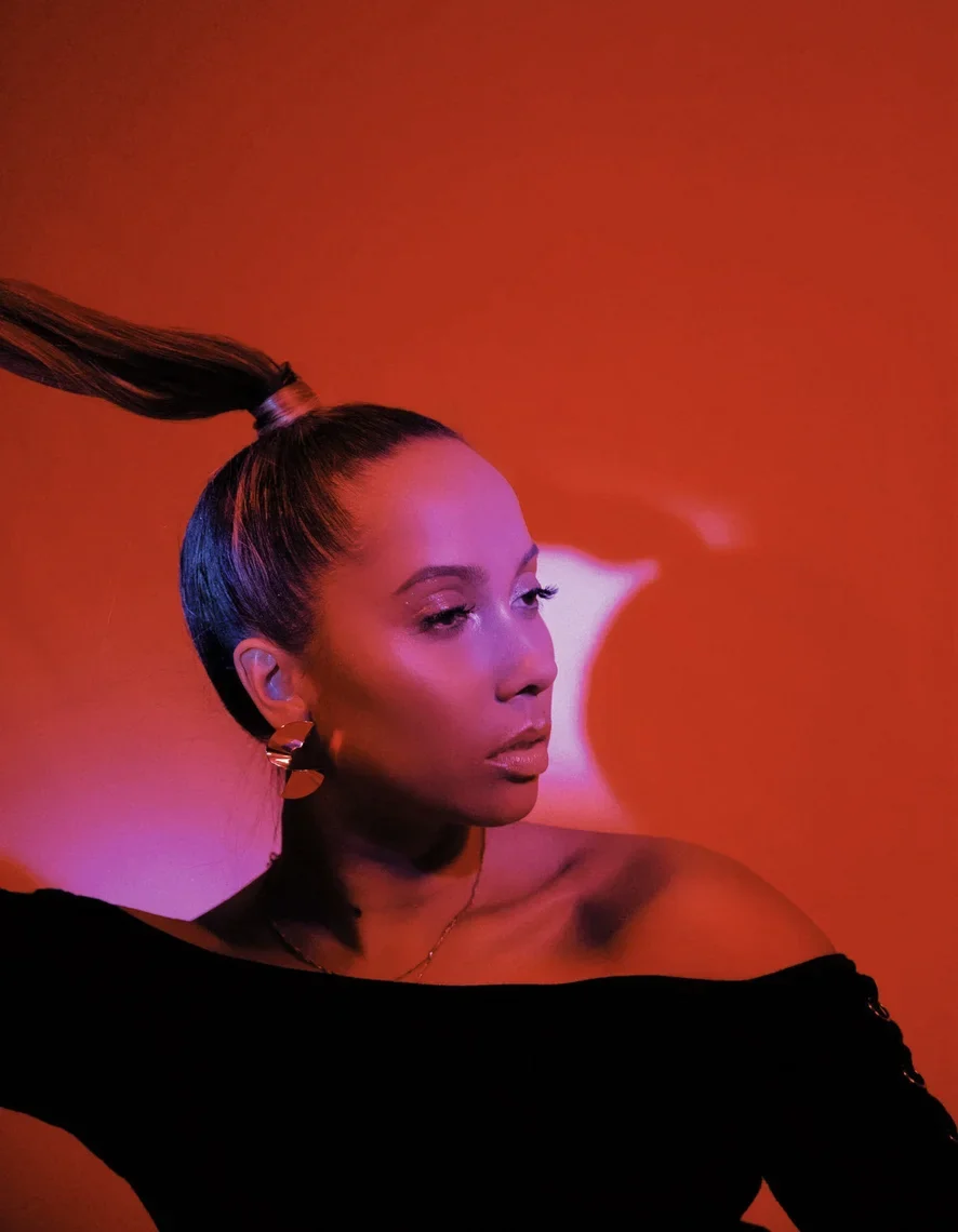 ROMII in profile against a red wall, hair pulled into a high ponytail