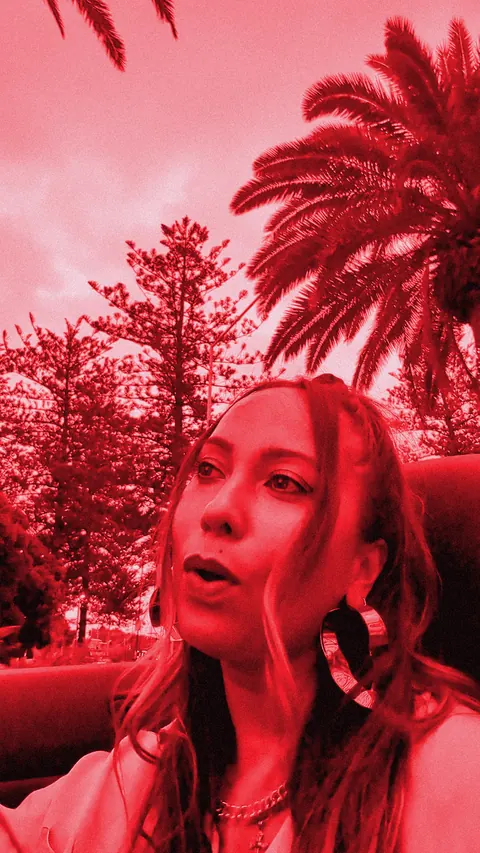 ROMII singing in a convertible beneath palm trees, red-toned still